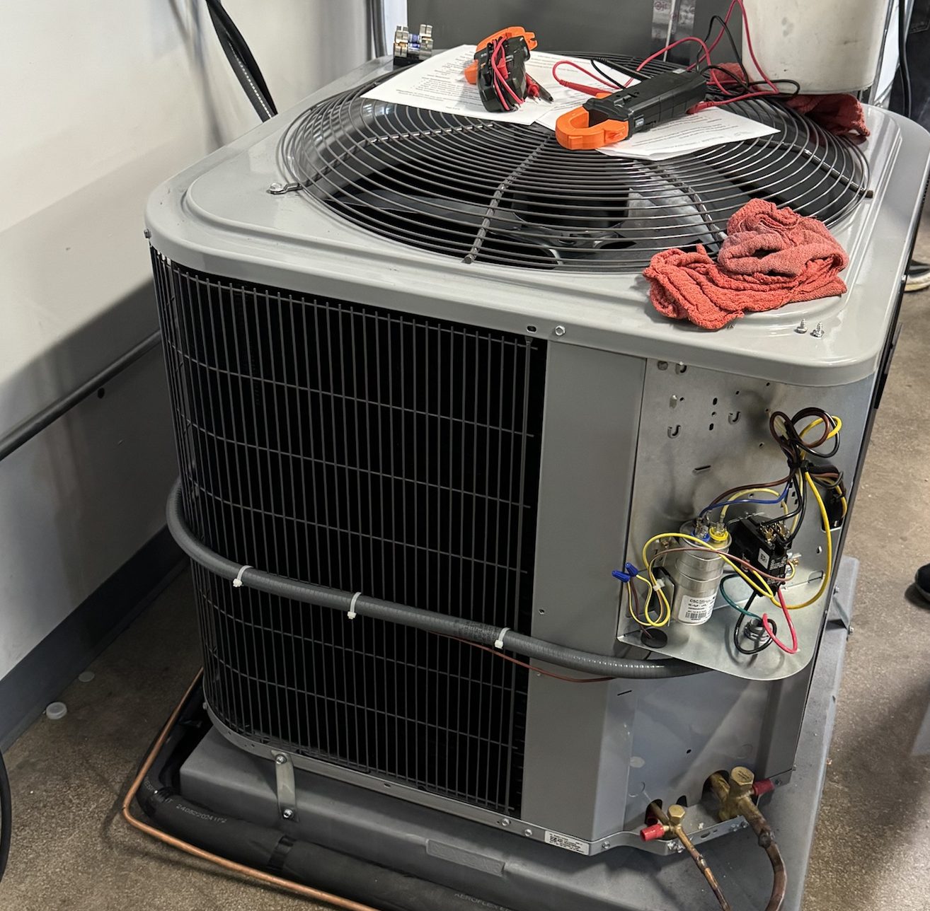 Outdoor air conditioner condenser being serviced, with a clamp meter on top