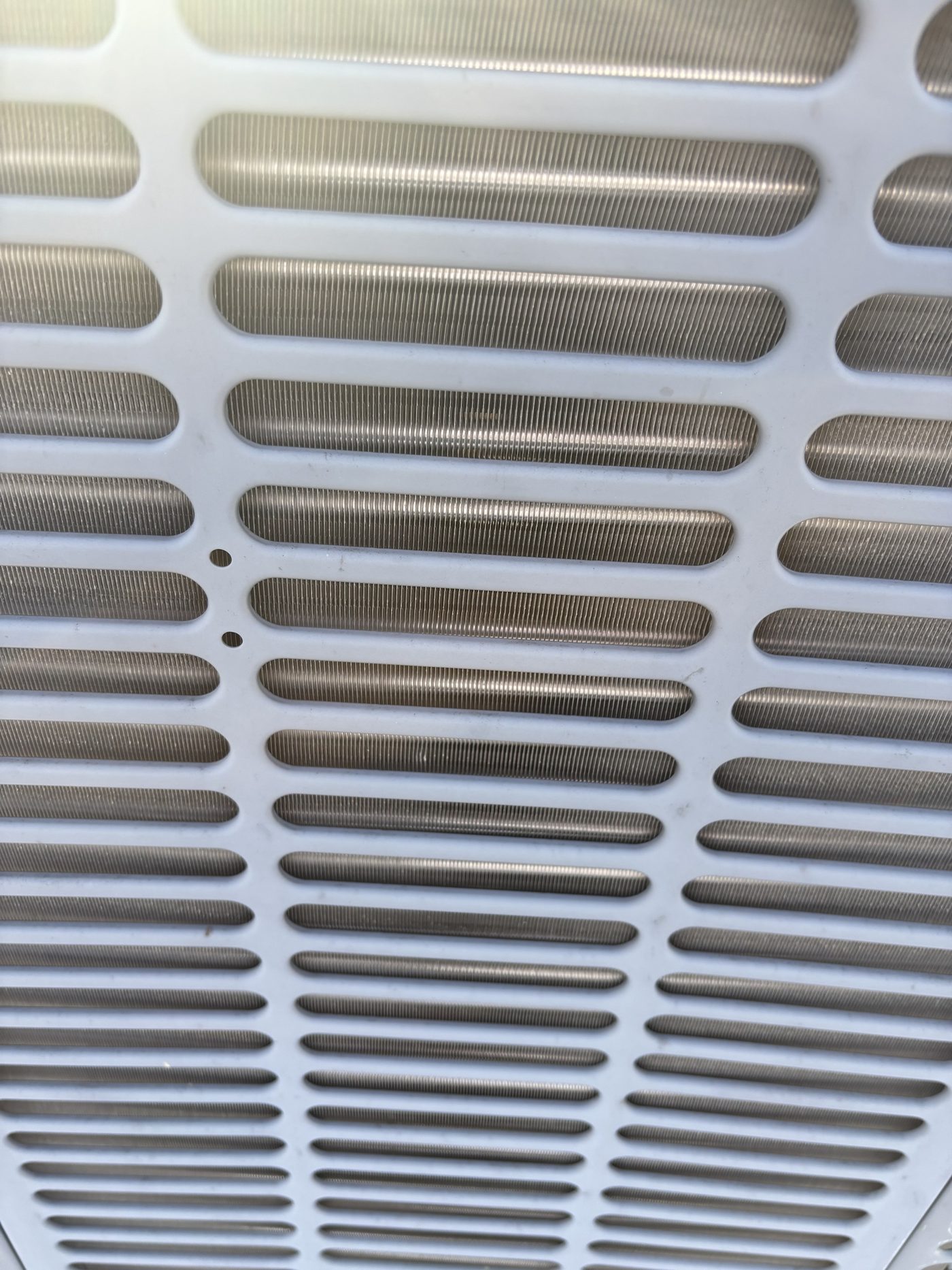 Close-up of a clean outdoor AC condenser coil behind the unit grille